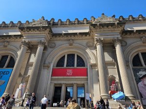 Front façade of the Metropolitan Museum of Art in NYC, featuring grand neoclassical columns, arched entrance, and a red banner above the main doors.