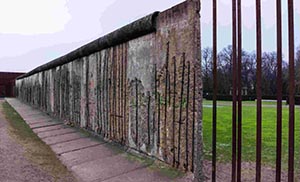 Historical view of the Berlin Wall with grass and trees in the background.