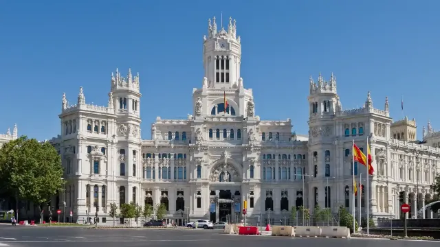 Main facade of the Madrid City Hall, a grand white building with tall towers and decorative sculptures, set against a clear blue sky.